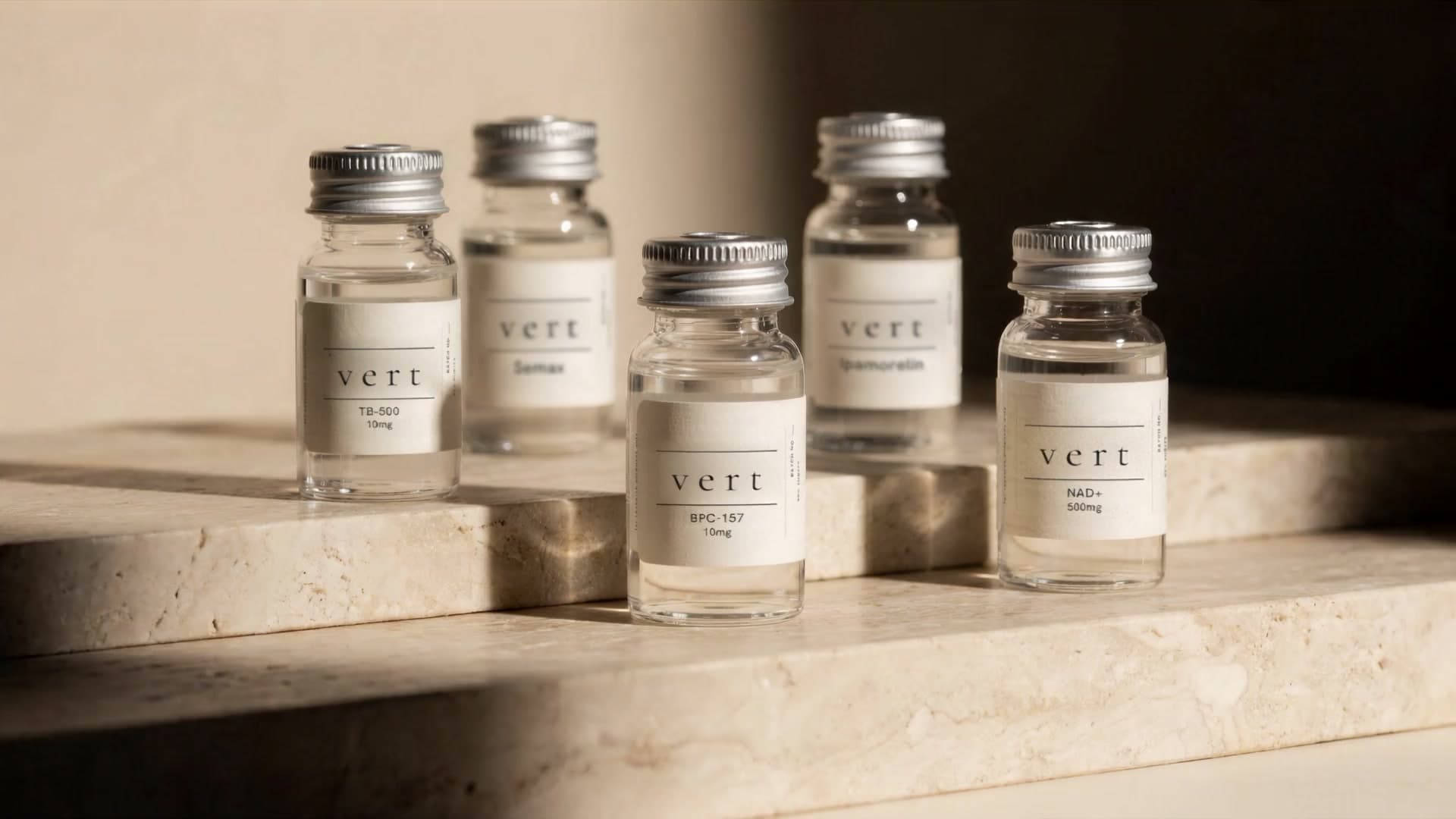 Five VERT research peptide vials on a travertine ledge as afternoon light drifts across them